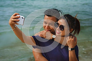 Summer holidays lifestyle portrait of young happy and playful Asian Korean couple tourist enjoying at the beach taking selfie