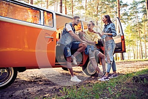 Summer holidays, road trip, vacation, travel and people concept - smiling young hippie friends having fun over minivan