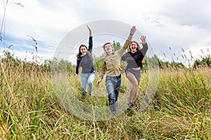 Summer holidays vacation happy people concept. Group of three friends boy and two girls running and having fun together outdoors.