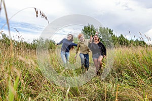 Summer holidays vacation happy people concept. Group of three friends boy and two girls running and having fun together outdoors.