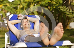 Summer holidays. Young man sunbathing. In the background a palm tree. Vacation concept. Man freelancer lies on a blue lounger.