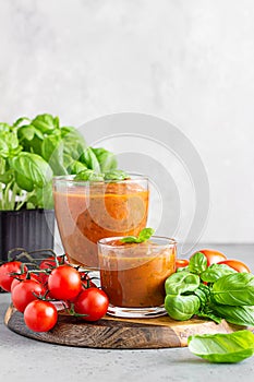 Summer homemade cold tomato cream soup in glass. Traditional Spanish soup gazpacho with basil. Grey concrete background