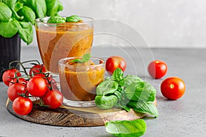 Summer homemade cold tomato cream soup in glass. Traditional Spanish soup gazpacho with basil. Grey concrete background