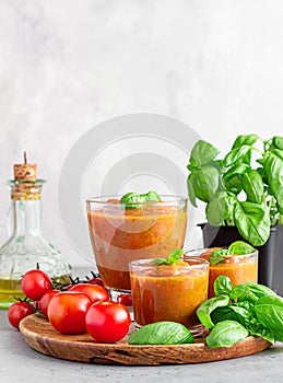 Summer homemade cold tomato cream soup in glass. Traditional Spanish soup gazpacho with basil. Grey concrete background