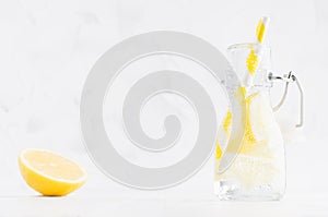 Summer homemade drink - infused lemon water with slices, soda, straw in yoke bottle in soft light white interior, copy space.