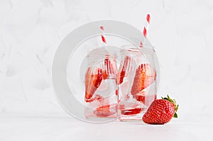 Summer homemade drinks - infused strawberry water with sliced berry, ice cubes, soda, straw in soft light white interior.