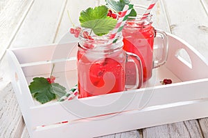Summer homemade red currant lemonade in a mason jar with decor of berry in tray on rustic table. Close up.