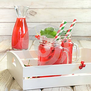 Summer homemade red currant lemonade in a mason jar with decor of berry in tray on rustic table. Close up.