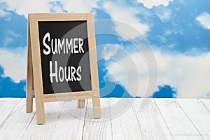 Summer Hours sign on standing chalkboard with sky