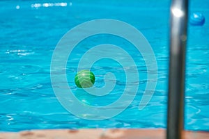 Summer image of a green rubber ball floating on the water of a pool