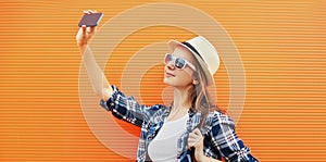 Summer image of young woman taking selfie picture by phone in the city over orange background