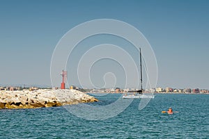 Rocky shore, blue sea, a man in a kayak, a white yacht with passengers, a clear blue sky