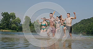 Summer joy group of happy friends having fun while running and splashing on river