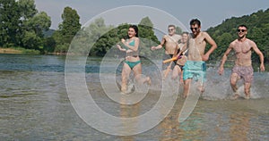 Summer joy group of happy friends having fun while running and splashing on river