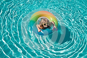 Summer kid swim at swimming pool. Funny happy child boy in swiming pool on inflatable rubber circle ring. Summertime