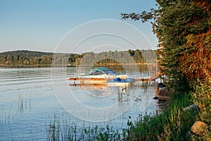 Summer on lake cottage. Small yacht boat by wooden dock pier on lake at sunset. Canadian Ontario Muskoka travel destination place