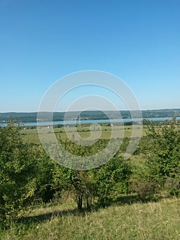 Summer landscape with agricultural field near the village on the lake