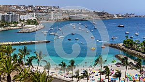 Summer landscape with a beach with people bathing, hotels and boats anchored in the sea. Gran Canaria. Arguineguin. Spain
