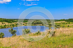 Summer landscape with beautiful lake, green meadows, hills, trees and blue sky