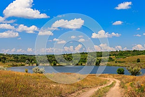 Summer landscape with dirt road to the lake and blue sky with white clouds