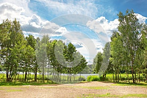 Summer landscape of green nature in bright sunny day. Blue sky with clouds over trees on lake.