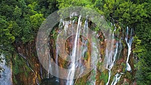 Summer landscape with high waterfall cascading over lush green cliff in dense forest. Mountain stream with clear water.