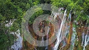 Summer landscape with high waterfall cascading over lush green cliff in dense forest. Mountain stream with clear water.