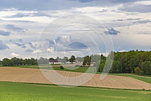 Summer landscape with hilly green field and farm in the distance