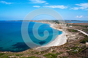 Summer landscape on the island of Sardinia. A small sandy beach, clear and blue sea, a dirt road and a small village in the backgr
