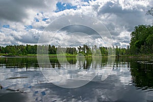 Summer landscape with lake and white cloud reflections in the water, tree silhouettes reflect in the lake water