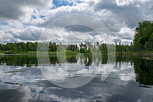 Summer landscape with lake and white cloud reflections in the water, tree silhouettes reflect in the lake water