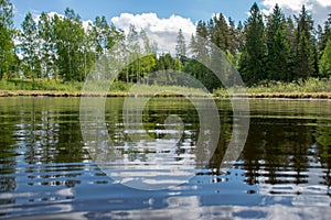 Summer landscape with lake and white cloud reflections in the water, tree silhouettes reflect in the lake water