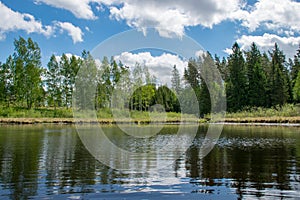 Summer landscape with lake and white cloud reflections in the water, tree silhouettes reflect in the lake water