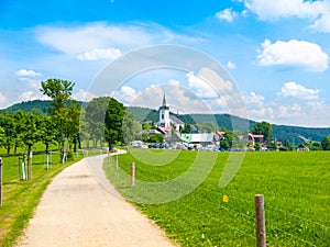 Summer landscape with lush green meadow, country road and white rural church. Prichovice, Northern Bohemia, Czech