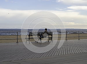 Summer Landscape with man sitting on the bench on Brighton Beach Boardwalk, skies and ocean during sunset , July, 2020.