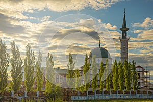 Summer landscape with mosque, minaret and pyramidal poplars in rays of sunset against blue cloudy summer sky.