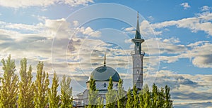 Summer landscape with mosque, minaret and pyramidal poplars in rays of sunset against blue cloudy summer sky.