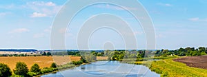 Summer landscape with river between fields. Wheat field and plowed field by the river. Panorama