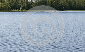 Summer landscape with a river, floating people on boats in the distance, green beach, smooth water