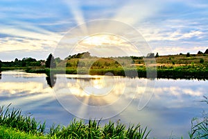 Summer landscape of sunset by the river with reflections