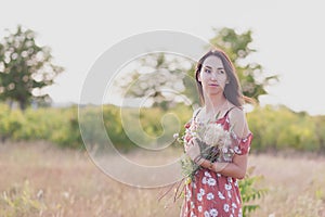 Summer lifestyle portrait of beautiful romantic girl holding bouquet of wild flowers