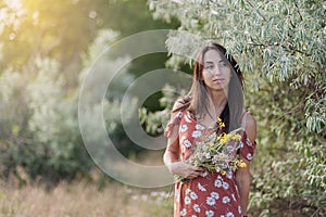 Summer lifestyle portrait of beautiful romantic girl holding bouquet of wild flowers