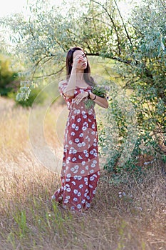 Summer lifestyle portrait of beautiful romantic girl holding bouquet of wild flowers