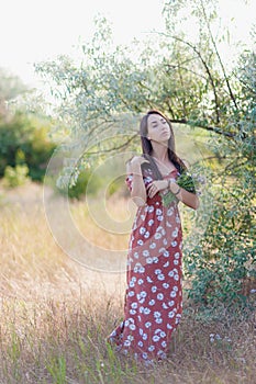 Summer lifestyle portrait of beautiful romantic girl holding bouquet of wild flowers