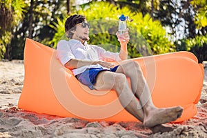 Summer lifestyle portrait of men sitting on the orange inflatable sofa drinking water on the beach of tropical island