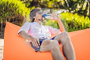 Summer lifestyle portrait of men sitting on the orange inflatable sofa drinking water on the beach of tropical island