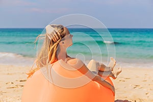 Summer lifestyle portrait of pretty girl sitting on the orange inflatable sofa on the beach of tropical island. Relaxing