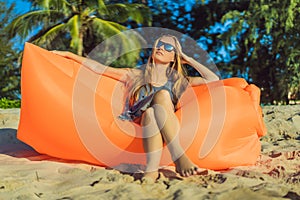 Summer lifestyle portrait of pretty girl sitting on the orange inflatable sofa on the beach of tropical island. Relaxing