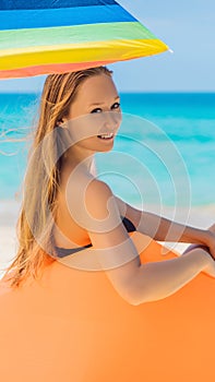 Summer lifestyle portrait of pretty girl sitting on the orange inflatable sofa on the beach of tropical island. Relaxing