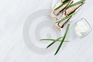 Summer light open sandwiches on crisps bread with fish preserves, feta cheese, green onion sprig on soft light white wood board.